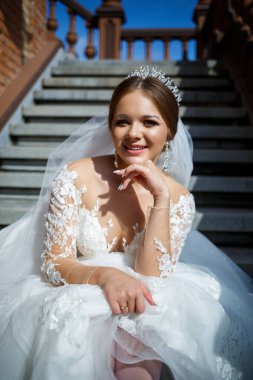 Beyaz gelinlikli güzel gelin merdivenlerde oturur ve güzel bir şekilde gülümser.