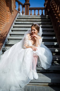 Beyaz gelinlik ve beyaz spor ayakkabılar içinde gelin büyük bir binanın merdivenlerinde oturuyor.
