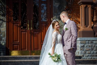 Beyaz gelinlik içinde gelin ve büyük adımlı tuğla bir binanın arka planında damat.