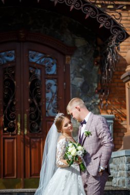 Beyaz gelinlik içinde gelin ve büyük adımlı tuğla bir binanın arka planında damat.