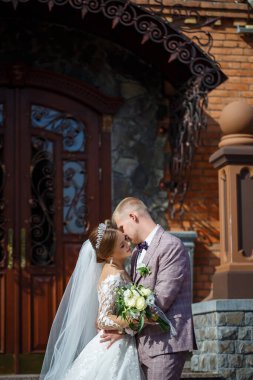 Beyaz gelinlik içinde gelin ve büyük adımlı tuğla bir binanın arka planında damat.