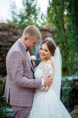 Beyaz elbiseli gelin ve kostümlü damat sarılıp parkta yürüyün.