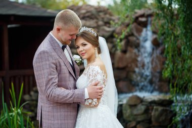 Beyaz elbiseli gelin ve kostümlü damat sarılıp parkta yürüyün.