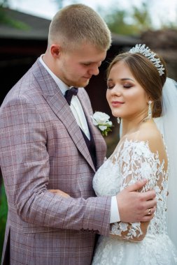 Beyaz elbiseli gelin ve kostümlü damat sarılıp parkta yürüyün.