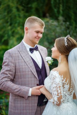 Beyaz elbiseli gelin ve kostümlü damat sarılıp parkta yürüyün.