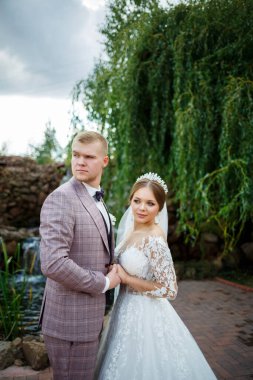 Beyaz elbiseli gelin ve kostümlü damat sarılıp parkta yürüyün.