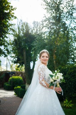 Beyaz elbiseli gelin ellerinde buket ve kafasında taçla.
