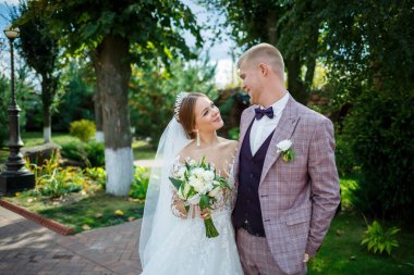 Beyaz elbiseli gelin ve kostümlü damat sarılıp parkta yürüyün.