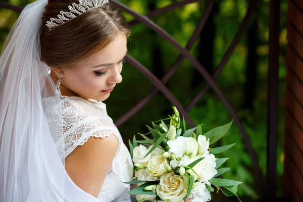 美しい花嫁のベールと白いコートは彼女の手に結婚式の花束と毛布の上に座っている — ストック写真