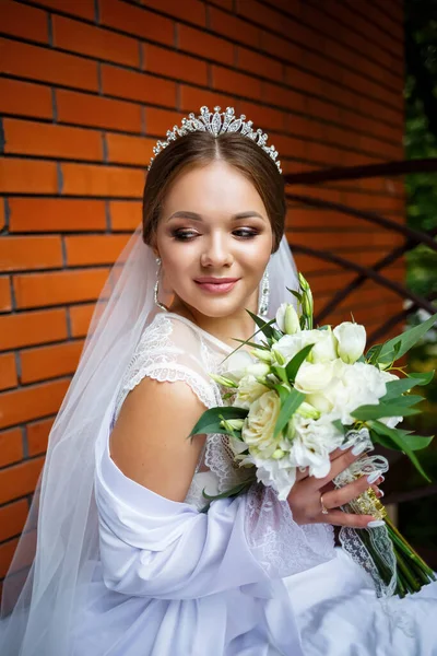 Duvak takmış güzel bir gelin ve elinde bir buketle bir battaniyenin üzerinde oturan beyaz bir ceket.