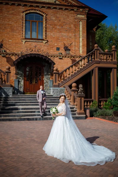 Beyaz gelinlik içinde gelin ve büyük adımlı tuğla bir binanın arka planında damat.