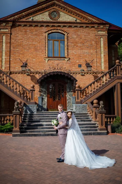 Beyaz gelinlik içinde gelin ve büyük adımlı tuğla bir binanın arka planında damat.