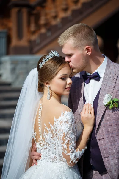 Beyaz gelinlik içinde gelin ve büyük adımlı tuğla bir binanın arka planında damat.