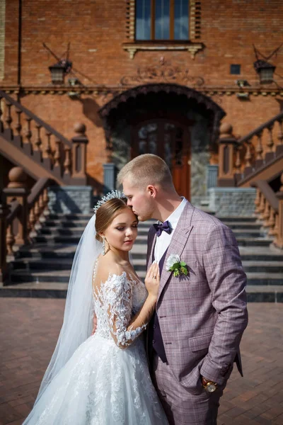 Beyaz gelinlik içinde gelin ve büyük adımlı tuğla bir binanın arka planında damat.