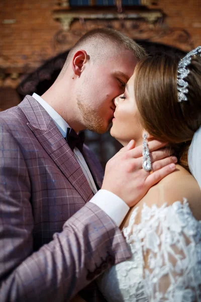 Beyaz gelinlik içinde gelin ve büyük adımlı tuğla bir binanın arka planında damat.