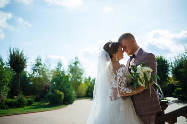 Beyaz elbiseli gelin ve kostümlü damat sarılıp parkta yürüyün.