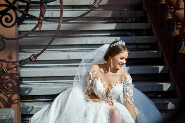 Beyaz gelinlikli güzel gelin merdivenlerde oturur ve güzel bir şekilde gülümser.