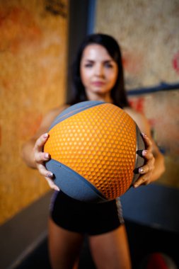 Spor salonunda elinde spor topuyla siyah takım elbiseli bir kız.