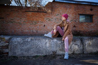 Şehir harabelerinde kahverengi ceketli, pembe takım elbiseli ve gri çizmeli şık kız mankeni. Modern moda eğilimleri. Moda görüntüsü