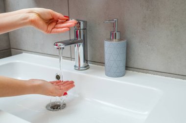 Banyoda gümüş musluğu olan beyaz lavabo. Ellerinde sıvı sabun olan gri teneke kutu. Musluk suyunu açmak, kişisel el hijyeni. Akan suyun altında el yıkama
