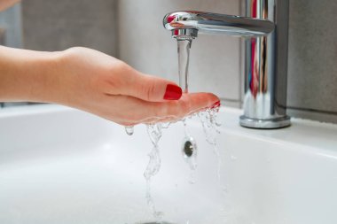 Banyoda gümüş musluğu olan beyaz lavabo. Ellerinde sıvı sabun olan gri teneke kutu. Musluk suyunu açmak, kişisel el hijyeni. Akan suyun altında el yıkama