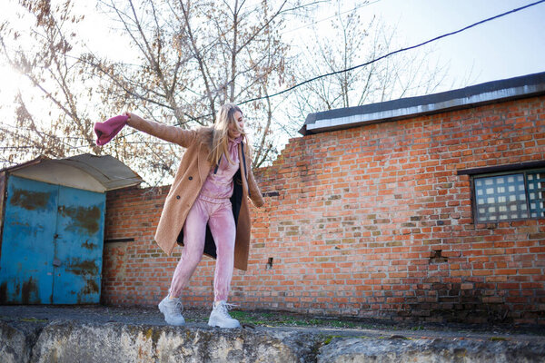 стильная девушка модель в коричневом пальто, розовый костюм и серые сапоги на руинах города. Современные тенденции моды. Модный образ
