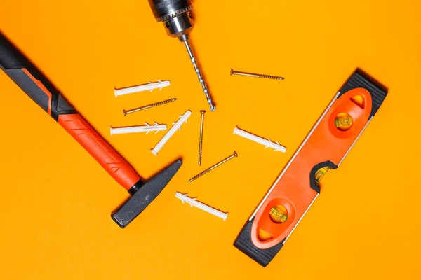 Tools for repairing home use. Hammer for nails, level and drill, dowel in the wall on an orange background. Toolkit for the wizard