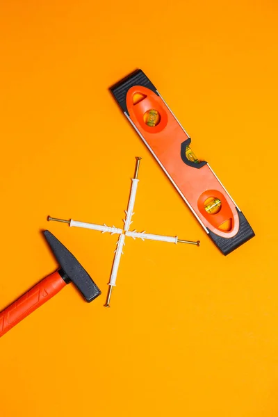 Tools for repair. Hammer for nails, level, dowel in the wall on an orange background. Toolkit for the wizard