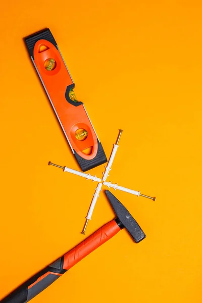 Tools for repair. Hammer for nails, level, dowel in the wall on an orange background. Toolkit for the wizard