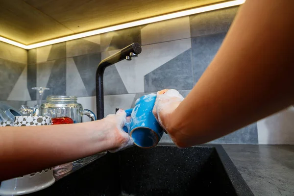 Hands with sponge wash the cup under water, housewife woman in washing blue mug in a kitchen sink with a blue sponge, Hand cleaning, manually, housework dishwasher