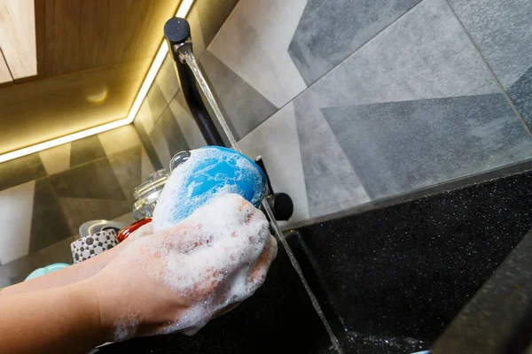 Hands with sponge wash the cup under water, housewife woman in washing blue mug in a kitchen sink with a blue sponge, Hand cleaning, manually, housework dishwasher