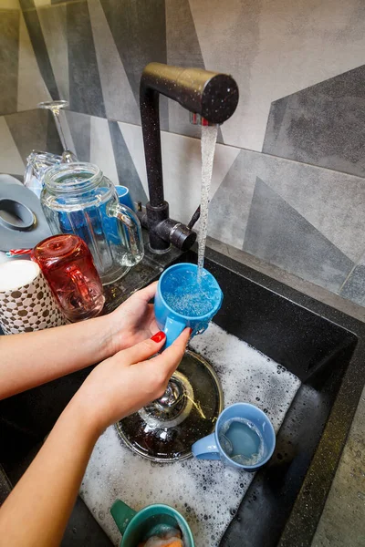 Hands with sponge wash the cup under water, housewife woman in washing blue mug in a kitchen sink with a blue sponge, Hand cleaning, manually, housework dishwasher