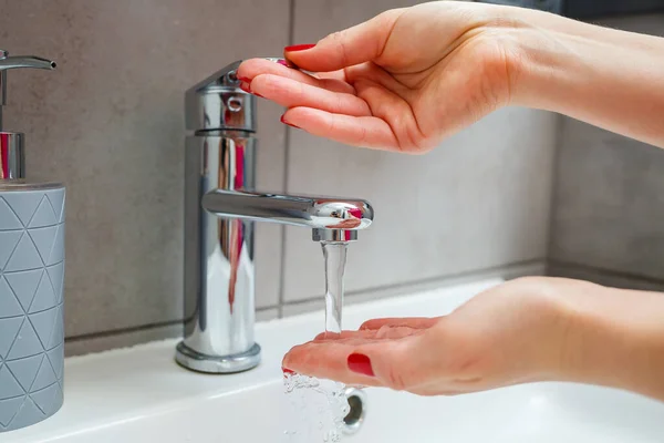 White sink with a silver faucet in the bathroom. Gray can with liquid soap for hands. Turning on the tap water, personal hand hygiene. Hand washing under running water