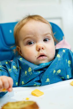 Küçük bir çocuk beslenme koltuğunda oturur ve ilk kez ekmek yer. Kırıntılarda yüz