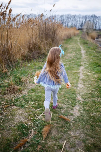 小女孩手里拿着干枯的芦苇 沿着一条森林小径跑着 春天里阳光灿烂 孩子的微笑和欢乐 — 图库照片