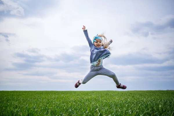 小女孩又跑又跳 田野绿草 春天里阳光明媚 孩子的微笑和欢乐 蓝天乌云密布 — 图库照片