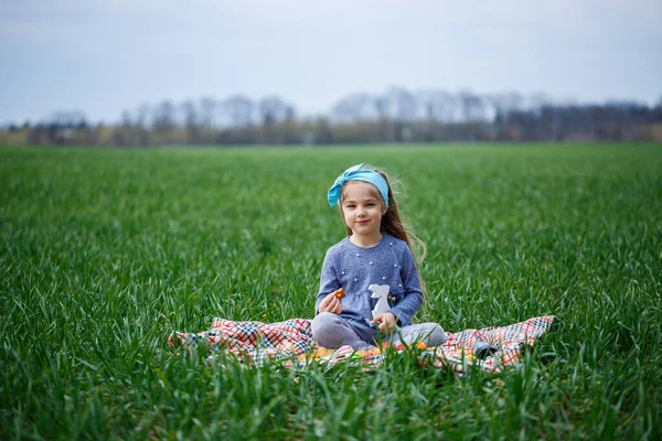 小女孩坐在床罩上 吃饼干和橘子酱 田里的青草 春天里阳光明媚 孩子的微笑和欢乐 蓝天乌云密布 — 图库照片