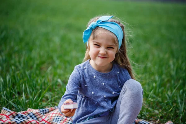 小さな女の子の子供はベッドの上に座ってクッキーやマーマレードを食べます フィールド内の緑の草 晴れた春の天気 子供の笑顔と喜び 雲と青空 — ストック写真