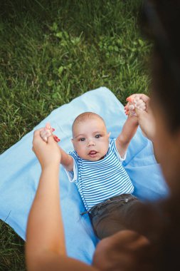 3 aylık küçük bir çocuk, yeşil çimlerin ve ağaçların etrafındaki mavi bir yatak örtüsünün üzerinde sırt üstü yatıyor. Çocukların sevinç duyguları