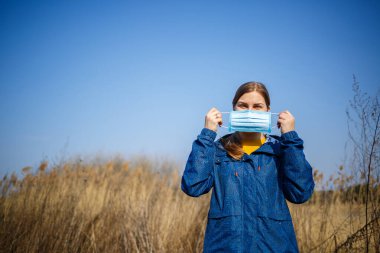 Dışarıdaki cerrahi maskeli, lastik kulaklıklı Portre Kadını kapatın. Ağız ve burnu örtmek için tipik 3 katlı cerrahi maske. Bakterilerin prosedür maskesi. Koruma kavramı.