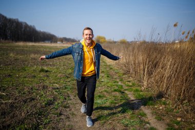 Gülümseyen adam ormanda esen rüzgardan zevk alıyor. Doğada yürürken mutlu bir adam, yeşil ağaçların arkasında boş bir alan. Hayat aşkı, neşe, temiz hava, yenileme konsepti