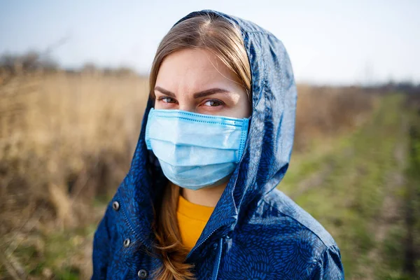 身穿蓝色夹克头罩的女孩戴着防护性医疗面罩 阳光明媚的日子里 外面的面具蒙住了病毒的脸 病毒性疾病 — 图库照片