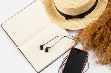 Cep telefonu, kulaklık, not defteri, şapka, yaşam tarzı, kadın, rahatla, kuru çim, dekor, düz yatak, beyaz arka plan tarzı. Seyahat, turizm konsepti. Plaj aksesuarları üst görünüm.