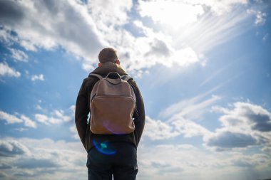 Omzunda sırt çantasıyla gezen turist beyaz bulutlu mavi gökyüzüne karşı, güneşli bir gün.