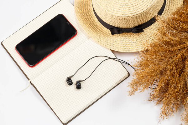 Mobile phone, headphones, notepad, hat, lifestyle, woman, relax, with dry grass, decor, flat lay, style on a white background. Travel, tourism concept. Beach accessories top view.