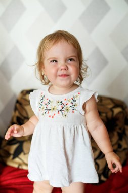 2 yaşında bir kız yatakta oturuyor ve gülümsüyor. Çocuk sevinir ve arkasını döner. Mutlu çocuk