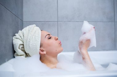 Kafasında beyaz havlu olan bir kız banyoda beyaz bir banyoda yatıyor. Bir sürü çamurlu sabunun ellerinde. Tam kıvrımlı köpük. Zor bir günün ardından rahatla. Spa rahatlatıcı tedavi