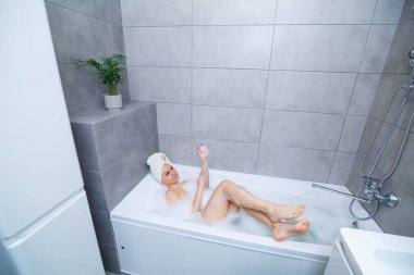Kafasında beyaz havlu olan bir kız banyoda beyaz bir banyoda yatıyor. Bir sürü çamurlu sabunun ellerinde. Tam kıvrımlı köpük. Zor bir günün ardından rahatla. Spa rahatlatıcı tedavi