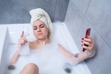 Kafasında havlu olan bir kız beyaz bir küvette bir bardak şampanyayla uzanıyor ve telefonda selfie çekiyor. Elinde bir sürü sarhoş sabunu var. Zor bir günün ardından rahatla. Spa gevşetici işlem