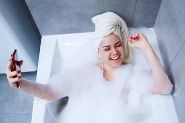Evde banyo yaparken müzik dinleyen ve şarkı söyleyen güzel bir genç kadın. Zor bir günün ardından rahatla. Spa gevşetici işlem.